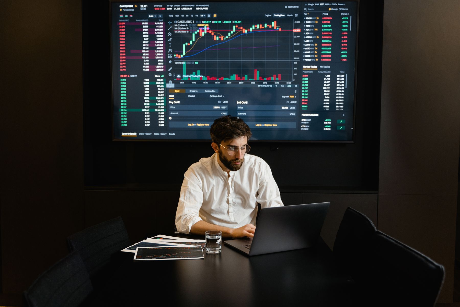 Financial analyst working at a laptop beneath a large market data display