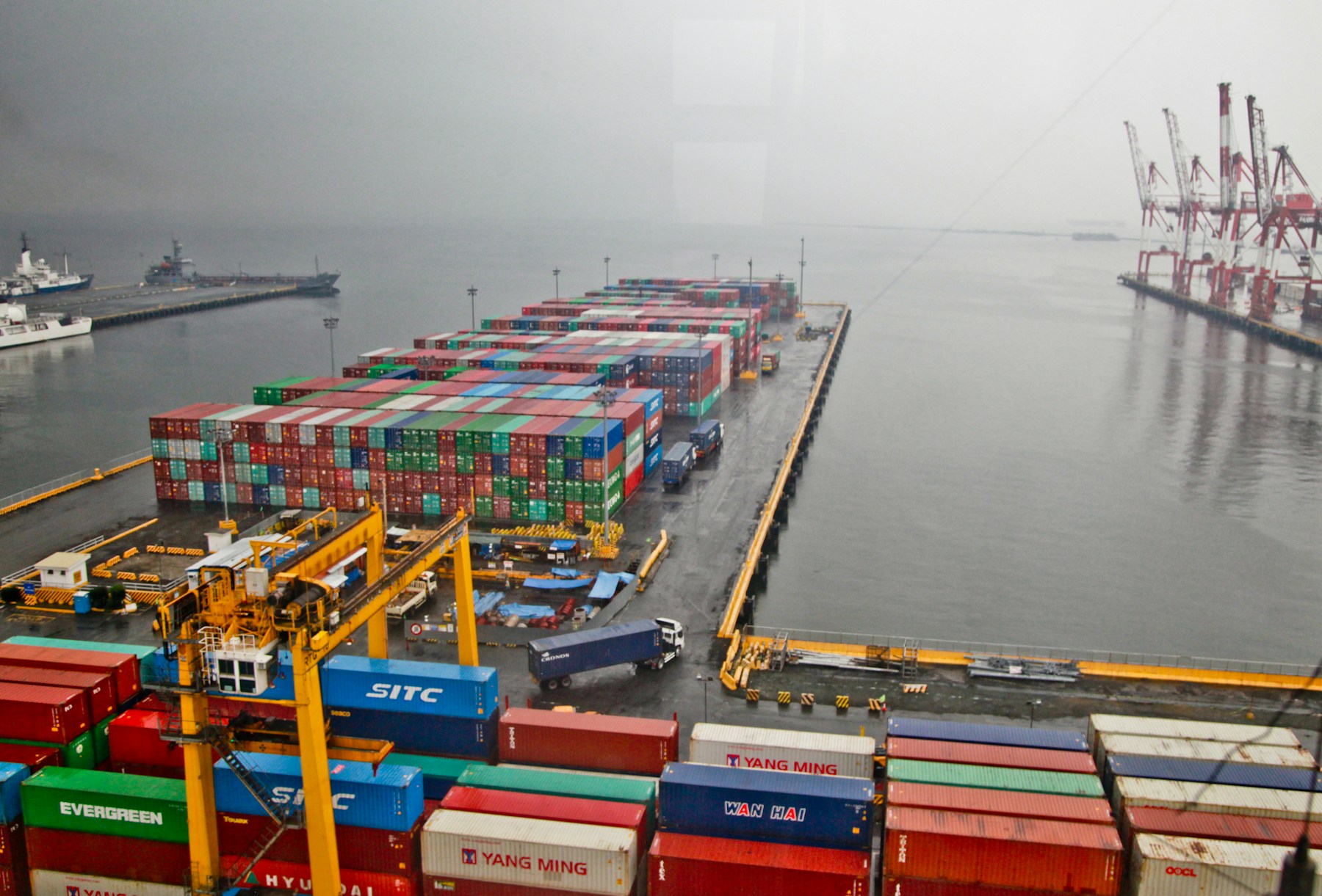 Shipping containers and yellow gantry cranes beside a cargo ship at a waterfront terminal